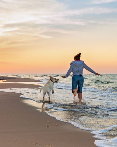 Photo d'une femme qui cours sur la plage avec son chien